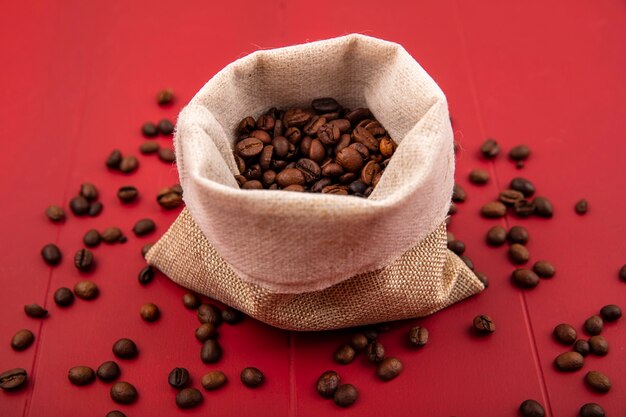 Vue de dessus des grains de café torréfiés frais sur un sac en toile de jute avec des grains de café isolé sur fond rouge