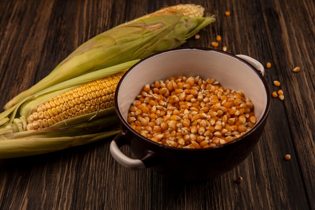 Photo gratuite vue de dessus des grains de maïs sur un bol avec du maïs frais sur une table en bois