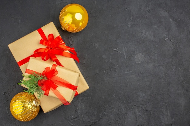 Vue de dessus grands et petits cadeaux de Noël en papier brun attaché avec des boules de ruban rouge sur une surface sombre