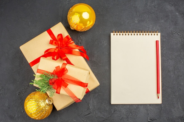 Vue de dessus grands et petits cadeaux de Noël en papier brun attaché avec un crayon de cahier de boules de ruban rouge sur une surface sombre