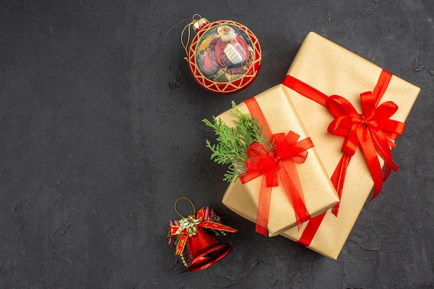 Vue de dessus grands et petits cadeaux de Noël en papier brun attaché avec des jouets d'arbre de Noël en ruban rouge sur fond sombre