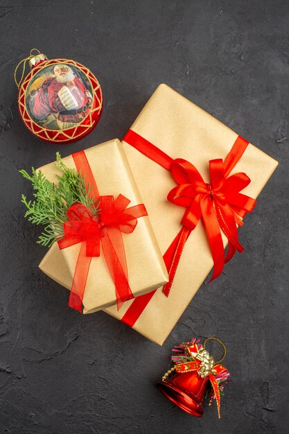 Vue de dessus grands et petits cadeaux de Noël en papier brun attaché avec des jouets d'arbre de Noël en ruban rouge sur une surface sombre