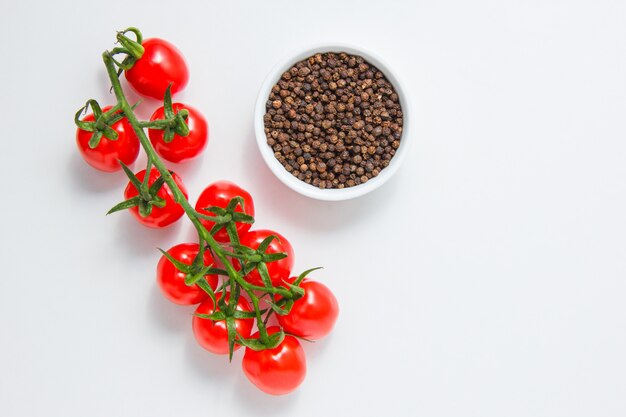 Vue de dessus des grappes de tomates avec un bol de poivre noir sur fond blanc. horizontal
