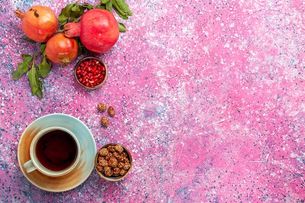 Vue de dessus de la grenade fraîche avec des feuilles vertes et une tasse de thé sur la surface rose