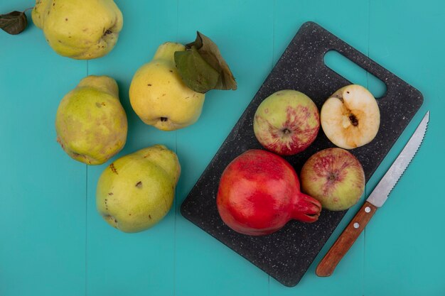 Vue de dessus de la grenade fraîche et des pommes sur une planche de cuisine noire avec couteau avec coings isolé sur fond bleu