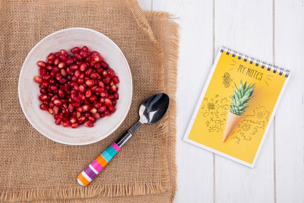 Vue de dessus de la grenade pelée sur une assiette avec une cuillère à café sur une serviette beige avec un ordinateur portable sur une surface blanche