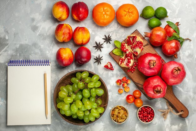 Vue de dessus des grenades rouges fraîches fruits aigres et moelleux avec des raisins verts frais sur le bureau blanc clair