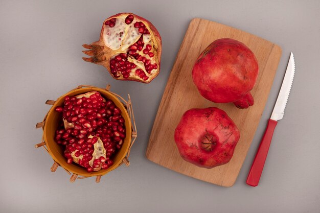 Vue de dessus des grenades rouges fraîches sur une planche de cuisine en bois avec un couteau avec des graines de grenade sur un bol