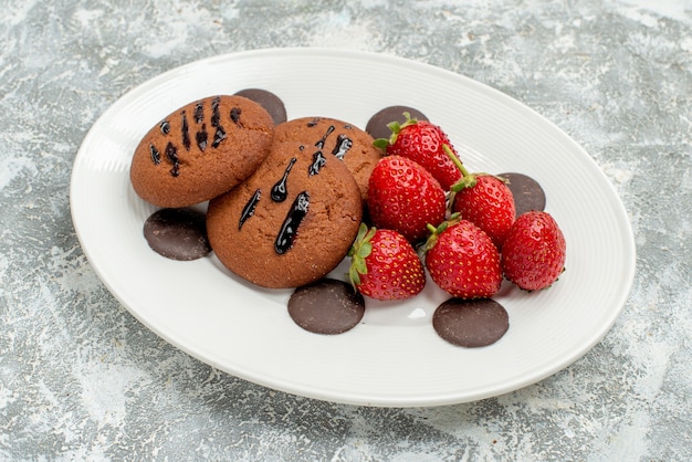 Vue de dessus Gros plan fraises biscuits au chocolat et chocolats ronds sur la plaque ovale blanche sur le sol gris-blanc