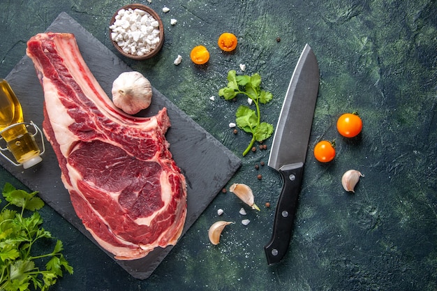 Vue de dessus grosse tranche de viande viande crue avec des verts sur une surface sombre