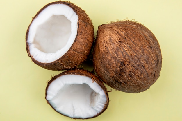 Vue de dessus de grosses noix de coco entières et coupées en deux sur une surface jaune