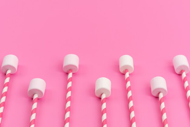 Une vue de dessus des guimauves blanches avec des bâtons roses sur un bureau rose, couleur sucrée de sucre