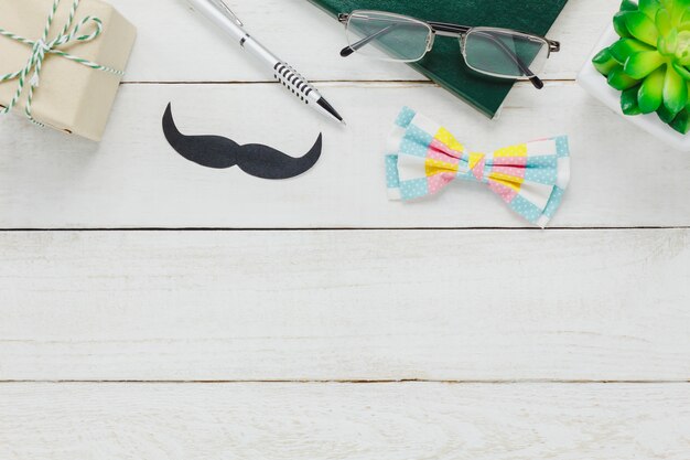 Vue de dessus Happy Father day.accessories avec arbre, moustache, cravate vintage, cadeau, stylo, cahier et lunettes sur fond de bois blanc rustique.