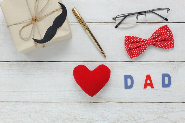 Vue de dessus Happy Father day .Red heart and word &quot;DAD&quot; sur fond de bois rustique. Accessoires avec moustache, cravate vintage, stylo, cadeau et lunettes.