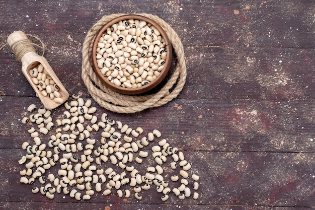 Vue de dessus des haricots crus frais à l'intérieur et à l'extérieur du bol brun répartis sur tout le haricot brun, haricot cru alimentaire