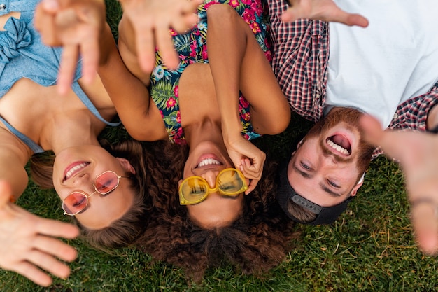 Vue de dessus d'en haut sur l'élégant coloré jeune entreprise heureuse d'amis allongé sur l'herbe dans le parc, l'homme et la femme s'amusant ensemble