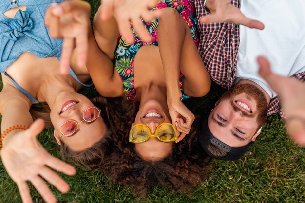 Vue de dessus d'en haut sur l'élégant coloré jeune entreprise heureuse d'amis allongé sur l'herbe dans le parc, l'homme et la femme s'amusant ensemble