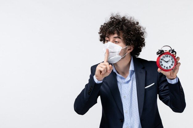 Vue de dessus d'un homme d'affaires en costume et portant son masque tenant une horloge faisant un geste de silence