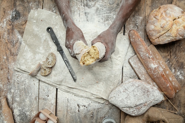 Vue de dessus de l'homme afro-américain cuisine des céréales fraîches, du pain, du son sur une table en bois