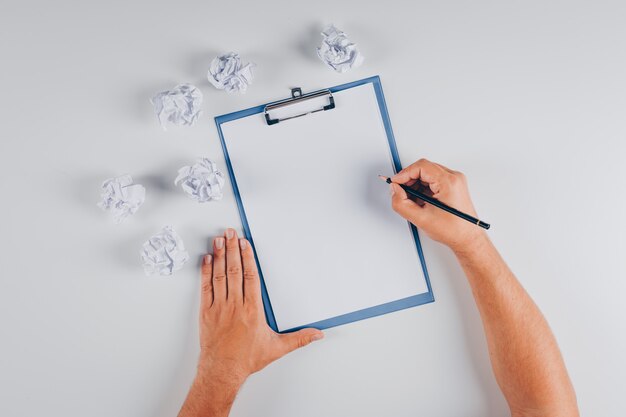 Vue de dessus l'homme écrit sur le presse-papiers avec des papiers froissés sur blanc