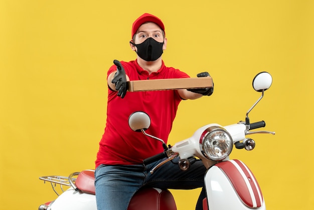 Vue de dessus de l'homme de messagerie portant un chemisier rouge et des gants de chapeau en masque médical assis sur un scooter donnant l'ordre