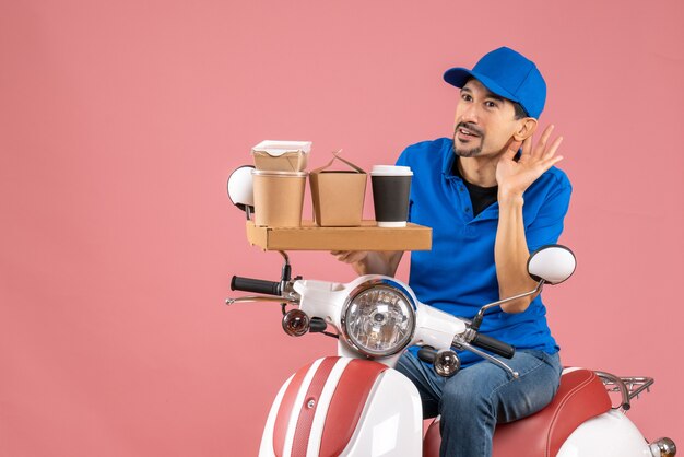 Vue de dessus de l'homme de messagerie surpris portant un chapeau assis sur un scooter écoutant les derniers commérages sur la pêche pastel