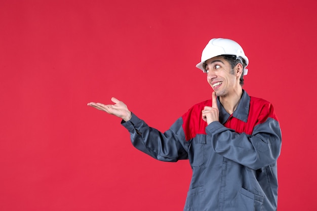 Vue de dessus d'un jeune architecte confus en uniforme avec un casque sur un mur rouge isolé