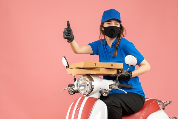 Vue de dessus d'une jeune coursière souriante portant un masque médical et des gants assis sur un scooter