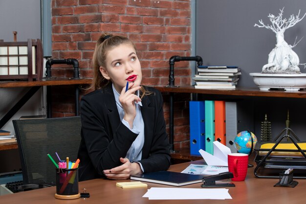 Vue de dessus d'une jeune employée de bureau incertaine et incertaine assise à son bureau et posant pour la caméra