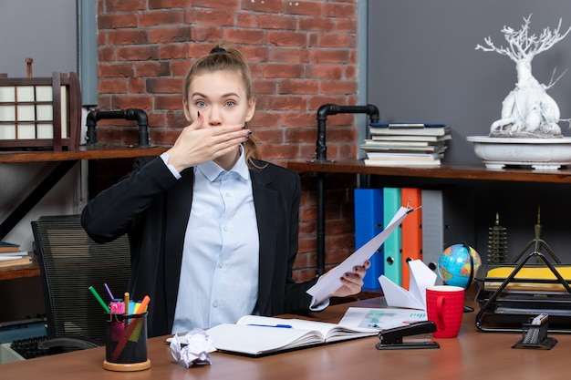 Vue de dessus d'une jeune femme assise à une table et tenant le document en bâillant au bureau