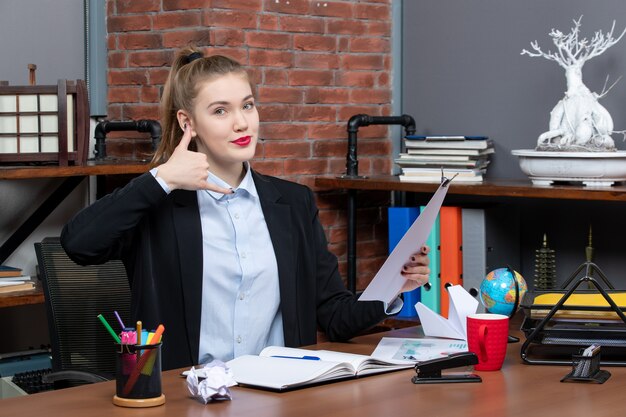 Vue de dessus d'une jeune femme assise à une table et tenant le document me faisant appeler le geste au bureau