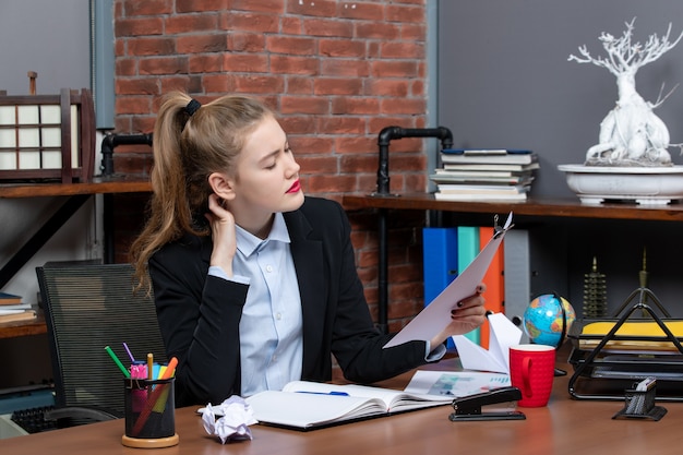 Vue de dessus d'une jeune femme assise à une table et tenant le document souffrant de maux de tête au bureau