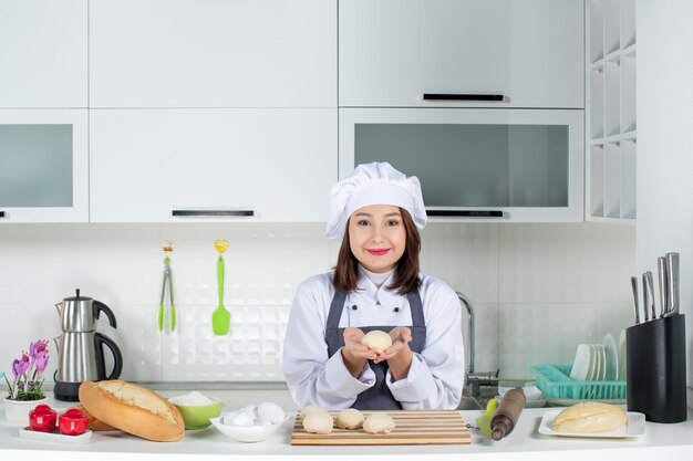 Vue de dessus d'une jeune femme chef souriante en uniforme debout derrière une table préparant la pâtisserie dans la cuisine blanche