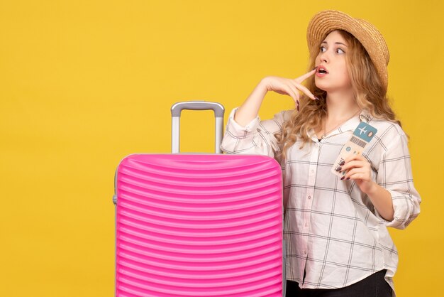 Vue de dessus de la jeune femme concentrée portant un chapeau montrant un billet et debout près de son sac rose