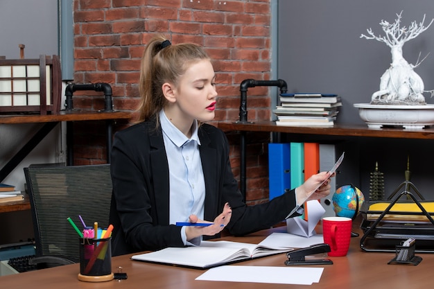 Photo gratuite vue de dessus d'une jeune femme confuse assise à une table et lisant un document au bureau