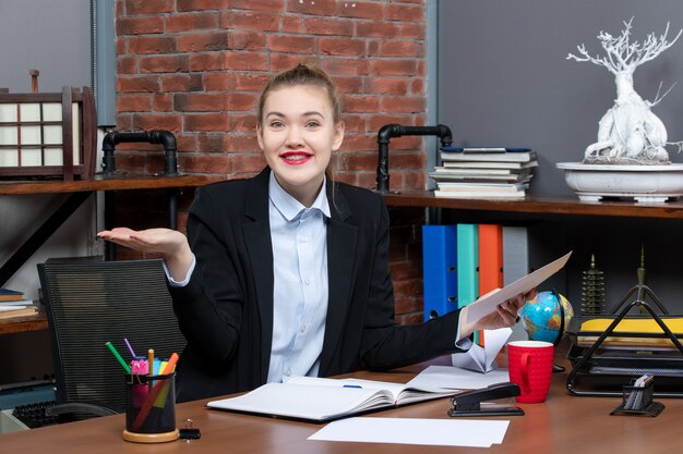 Vue de dessus d'une jeune femme curieuse assise à une table et tenant un document au bureau