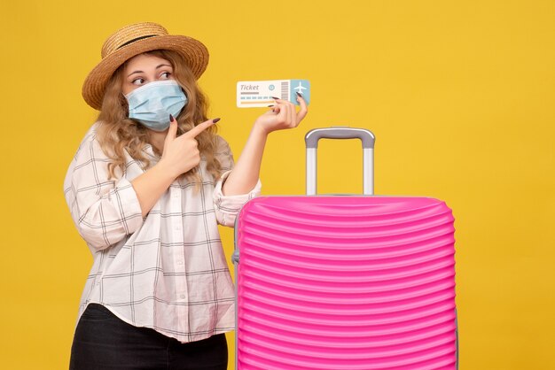 Vue de dessus de la jeune femme émotionnelle portant un masque de pointage et debout près de son sac rose