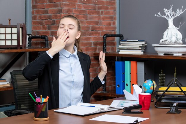 Vue de dessus d'une jeune femme endormie assise à une table et tenant le document en bâillant au bureau