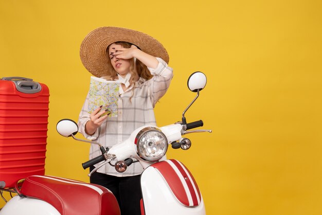 Vue de dessus de la jeune femme fatiguée portant un chapeau rassemblant ses bagages assis sur la moto et tenant la carte