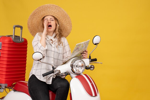 Vue de dessus de la jeune femme portant un chapeau et assis sur une moto et tenant une carte appelant quelqu'un sur jaune