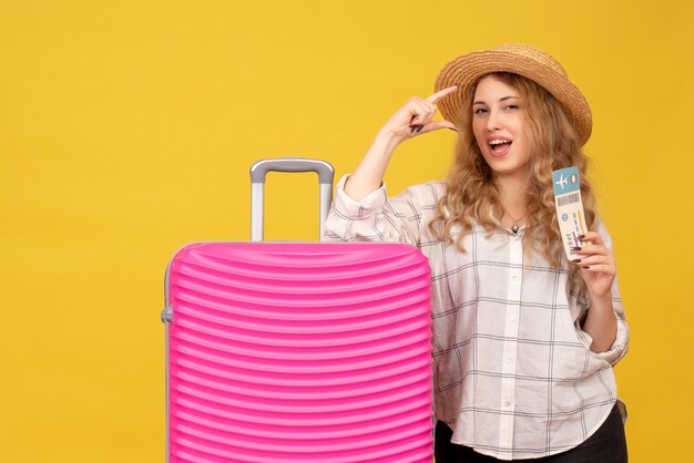 Vue de dessus de la jeune femme souriante portant un chapeau montrant un billet et debout près de son sac rose