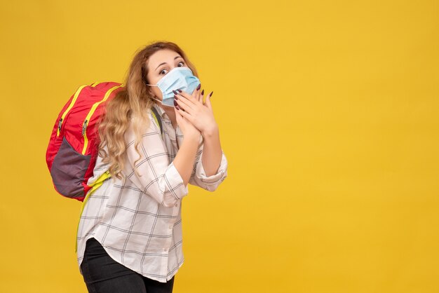 Vue de dessus de la jeune fille voyageuse surprise portant son masque et sac à dos sur jaune