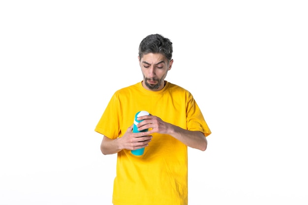 Vue de dessus d'un jeune homme concentré en chemise jaune tenant un thermos sur une surface blanche