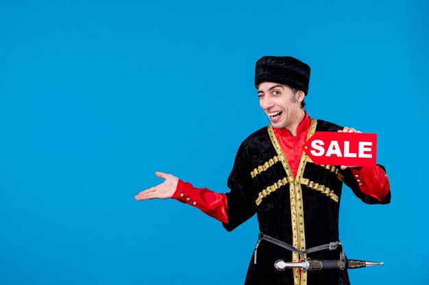 Vue de dessus d'un jeune homme drôle souriant en costume traditionnel montrant l'icône de vente et pointant quelque chose sur fond de vague bleue