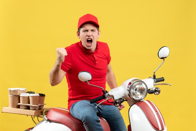 Vue de dessus d'un jeune homme émotionnel fier et ambitieux portant un chemisier rouge et un chapeau livrant des commandes sur fond jaune