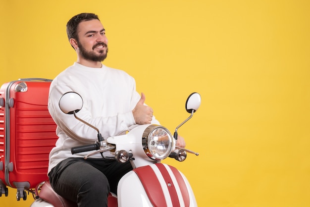 Vue de dessus d'un jeune homme souriant assis sur une moto avec une valise dessus et faisant un geste correct sur jaune