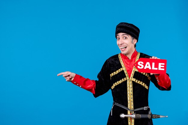 Vue de dessus d'un jeune homme souriant en costume traditionnel montrant l'icône de vente et pointant quelque chose sur fond de vague bleue