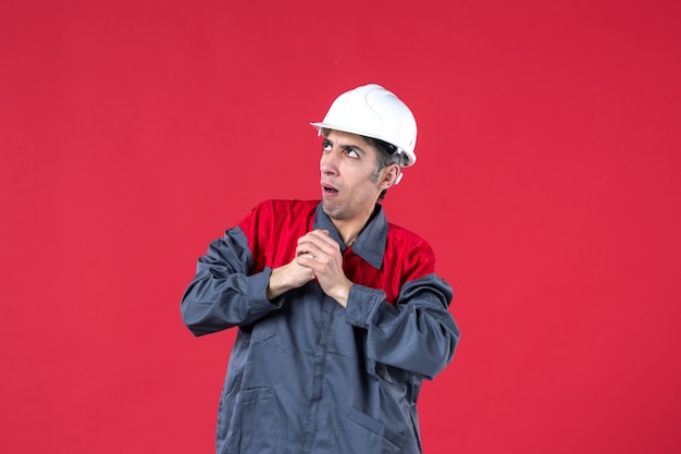 Vue de dessus d'un jeune travailleur confus en uniforme avec un casque sur un mur rouge isolé