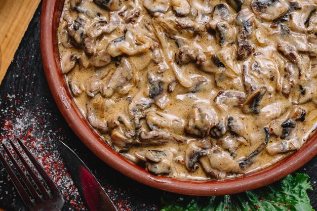 Vue de dessus julienne de champignons au four avec du fromage dans un plat d'argile sur une planche