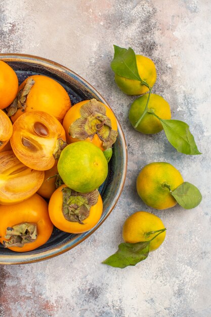 Vue de dessus des kakis frais dans un bol et des mandarines sur fond nude